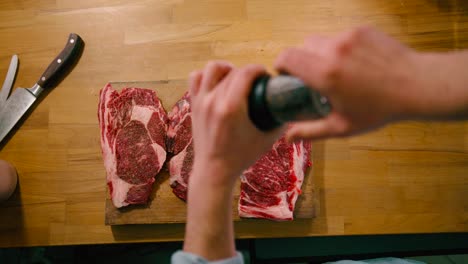 Draufsicht-Des-Mannes,-Der-Schwarzes-Pfefferkorn-Auf-Rotem-Köstlichem-Steakfleisch-Mahlt-Und-Sich-Zum-Kochen-Vorbereitet