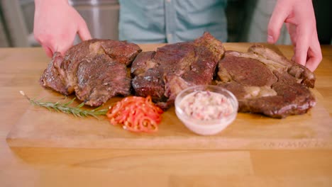 Man-with-a-grilled-marinated-beef-flank-steak-on-a-wooden-board-placed-on-the-table-ready-to-serve