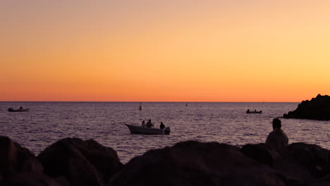 The-silhouette-of-fishermen-on-boat-off-shore-during-an-orange-sunset-with-sun-reflections-on-each-surface-of-the-Grand-Canary-island-valley-4k-slow-motion-capture-at-60fps...