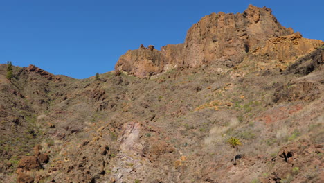 Der-Gipfel-Der-Rocker-Und-Die-Bewegung-Unten-Auf-Dem-Steinigen-Bergpfad,-Der-Unter-Einem-Berg-Auf-Der-Gran-Canary-Island-Führt-4k-zeitlupenaufnahme-Mit-60fps