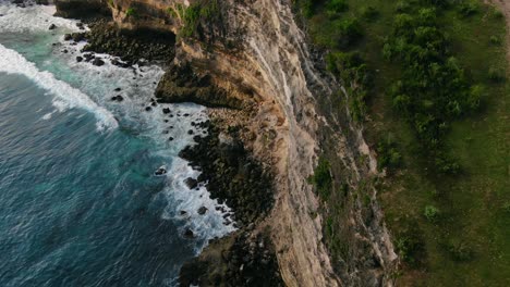 Bird’s-eye-view-moving-forward-shot,-rocky-cliffs-of-Tanjung,-green-grass-and-tree-on-the-top-of-the-cliff