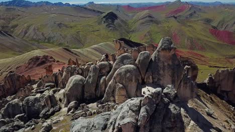 Aerial,-reverse,-drone-shot-away-from-a-man-standing-on-huge-rocks,-at-the-Palccoyo-rainbow-mountain,-in-Valle-Rojo-Valley,-Andes,-Peru,-South-America