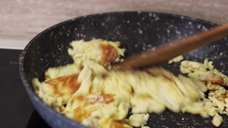 Scrambled-eggs-browning-in-black-skillet-with-wood-spatula,-close-up