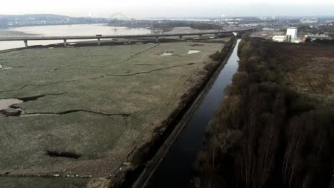 River-marsh-land-coast-commuter-traffic-crossing-bridge-uk-Aerial-pull-back-view