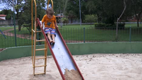kid-climbing-up-and-then-sliding-down-the-slide-with-sand-on-the-end-during-a-bright-day-with-trees-in-the-background