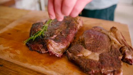 Close-up-view-of-a-man-applying-ghee-to-the-roasted-grilled-steaks-on-the-wooden-table