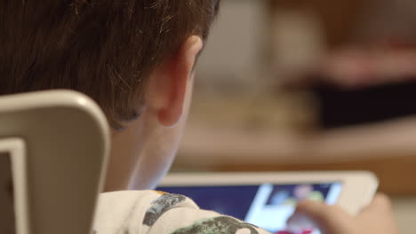 Over-the-shoulder-as-young-boy-watches-video-on-tablet,-close-up