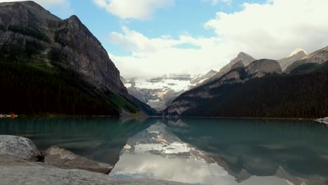 A-superb-timelapse-during-sunrise-made-with-an-DJI-Osmo-action-camera-of-Lake-Louise-in-Alberta,-with-clouds-passing-over-the-mountains-and-the-reflection-of-the-mountains-in-the-clear-water