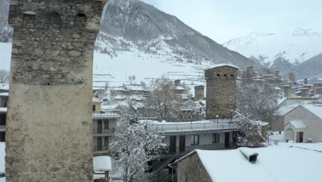 House-Roofs-And-Chimneys-And-Filled-With-Thick-White-Snow-In-Mestia,-Svaneti,-Georgia-On-A-Cold-Winter-Day-With-Majestic-Mountain-In-The-Background---Drone-Shot