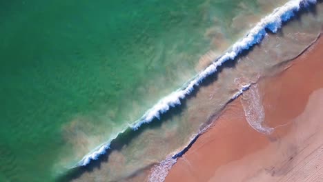 Aerial-overhead-ascending-shot-of-big-waves-reaching-the-beach