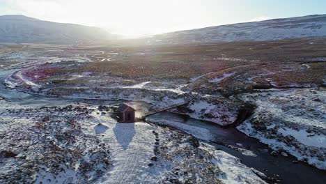 Impresionante-Paisaje-De-Casa-Solitaria-En-Un-Campo-Nevado-En-Islandia-Cerca-De-La-Corriente-Que-Fluye-En-Un-Brillante-Día-De-Invierno---Toma-Aérea-De-Drones