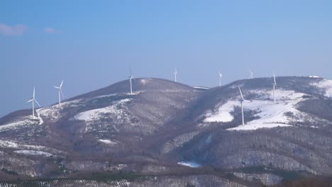 Hills-Covered-in-Snow-with-a-wind-turbine-farm-in-the-distance,-South-Korea