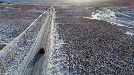 Cars-Driving-On-The-Asphalt-Road-Surrounded-By-Snowy-Fields-In-Iceland-With-Scenic-Mountains-And-Bright-Sun-In-The-Background---Aerial-Drone-Shot
