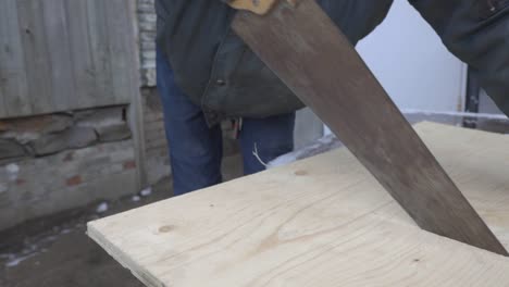 A-Man-Wearing-A-Black-Jacket-And-Gloves-Sawing-A-Big-Plank-Of-Wood