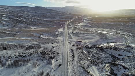 Driving-on-a-road-going-through-the-snowy-landscape-to-the-mountains-of-the-Phantom-Island-in-Iceland---aerial