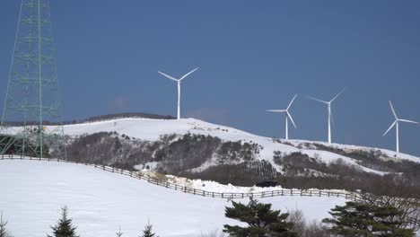 a-power-transmission-tower-and-many-wind-power-plants-are-seen-in-the-snow-covered-mountain,-South-Korea