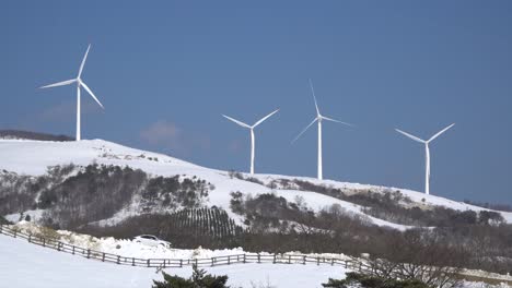 Winter-Austrian-alps-panorama-with-wind-turbines-farm,-mountain-peak-and-blue-sky-with-clouds-from-mountain-meadow