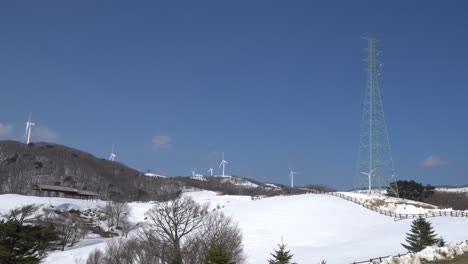 Wind-power-farm-and-power-transmission-tower-are-seen-in-the-mountain-in-winter,-South-Korea