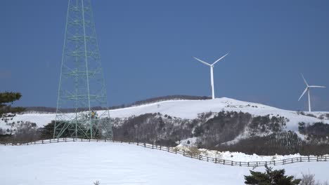 Wind-power-plants-and-power-transmission-tower-are-seen-in-the-mountain,-South-Korea
