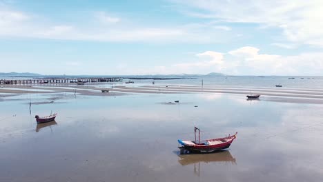 Traditional-fishing-boats-sitting-quietly-on-the-sandy-beach-during-low-tide-in-Thailand---low-aerial