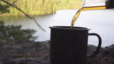 Pouring-freshly-brewed-coffee-into-mug-in-wilderness-with-spectacular-view-to-a-forest-and-river-from-a-slope