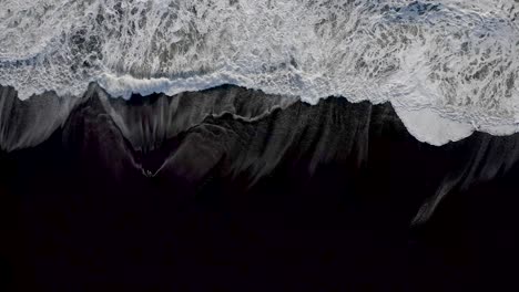 Waves-from-Atlantic-ocean-breaking-on-a-black-sand-beach,-top-down-aerial