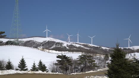 Power-transmission-tower-and-wind-turbines-and-pine-trees-are-seen-in-the-snow-covered-mountain-landscape,-Switzerland