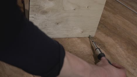 Human-hand-driving-screw-into-wooden-board---close-up-shot