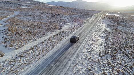 A-Black-Car-Driving-Carefully-On-The-Slippery-Road-Surrounded-By-Snowy-Fields-In-Iceland-On-A-Sunny-Morning---Aerial-Shot