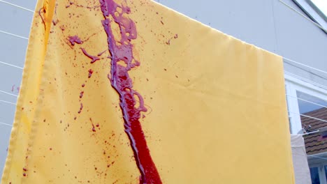 Slow-motion-shot-of-blood-splattering-over-a-yellow-sheet-hanging-on-a-washing-line