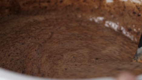 Stir-batter-for-chocolate-cake-with-spatula-in-white-bowl,-dripping-drops