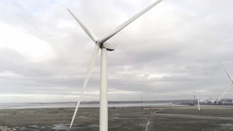 Nachhaltige-Elektrische-Windkraftanlagen,-Die-Sich-Auf-Englands-Ackerland-Drehen,-Steigen-Langsam-Zu-Rotorblättern-Auf,-Die-Sich-Am-Horizont-Drehen