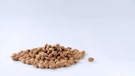 man-drops-a-hand-full-of-unroasted-almonds-on-a-pile,-then-grabs-a-hand-full,-white-reflective-background