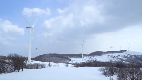 one-windmill-is-standing-near,-several-wind-power-plants-are-moving-and-generating-power-in-the-snow-covered-field-ranch,-South-Korea