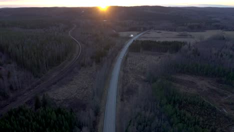 Reversed-drone-footage-flying-over-a-country-road-with-cars-driving-on-it-during-sunset