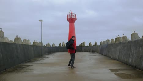 A-Man-Happily-Running-To-The-Red-Lighthouse,-So-called-Pier-Light,-At-The-Entrance-To-The-Port-Of-Kolobrzeg-In-Poland---wide-shot