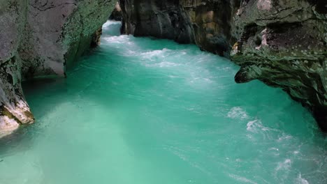 Dolly-in-of-clear-turquoise-Soca-River-flowing-between-limestone-walls-and-rocks-in-western-Slovenia