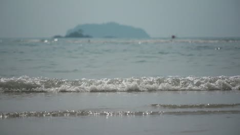 SLOW-MOTION,-Small-Ocean-Waves-Roll-In-With-Hazy-Mountain-In-The-Distance