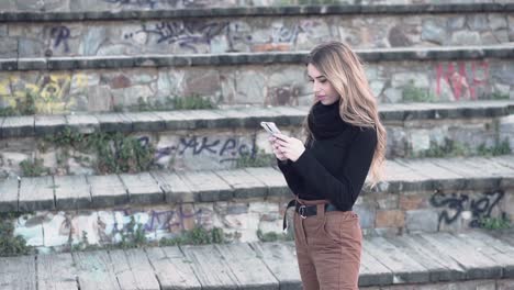 Slow-motion-video-of-a-young-blonde-caucasian-woman-standing-outdoors-texting-and-reading-messages-on-her-mobile-smart-phone