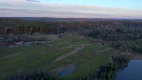 Reversed-drone-footage-showing-a-green-golf-course-during-the-winter-while-revealing-a-small-lake
