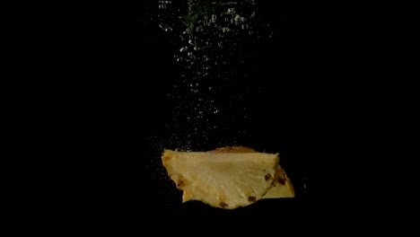 Two-juicy-slices-of-pineapple-falling-together-in-the-dark-clear-water