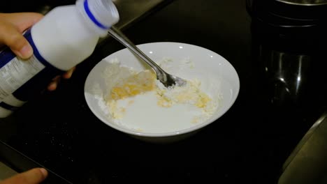 Pouring-Milk-into-bowl-of-Egg-and-Flour-and-Mixing-with-Spoon-Close-Up