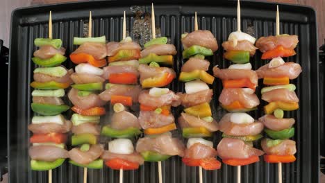Cenital-view-of-seven-chicken-and-vegetables-skewers-cooking-on-a-hot-electric-grill