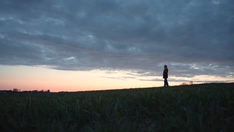 Girl-standing-on-a-field-looking-off-into-the-distance-at-sunset