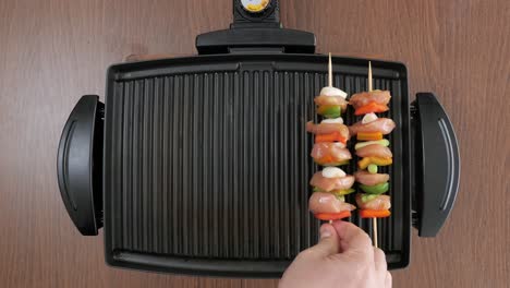 Man-putting-wooden-skewers-with-raw-chicken-and-vegetables-on-a-compact-electric-grill