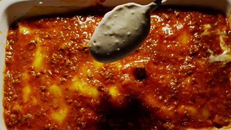 Overhead-view-of-bolognese-and-bechamel-sauce-being-pour-in-lasagana,-top-down