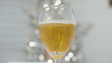 Hand-pouring-beer-into-a-glass-with-defocused-christmas-tree-in-the-background-in-slow-motion