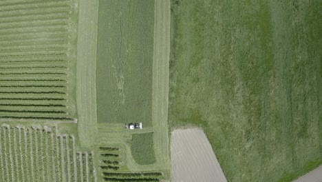 Tractor-moving-on-large-grass-field-in-South-Tyrol,-aerial-top-view