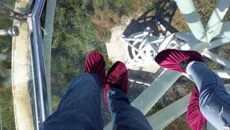 POV-Shot-Of-Two-People's-Feet-Wearing-Purple-Non-Slip-Shoes-Cover,-Walking-On-Glass-Skywalk-At-Phra-Yai-Phu-Khok-Ngio-Chiang-Khan-District,-Loei-Province-In-Thailand---High-Angle-Shot