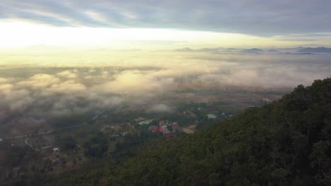 Drohne-Fliegt-über-Bewaldete-Berge-Mit-Ruhigem-Dorf-Am-Nebligen-Morgen-In-Thailand